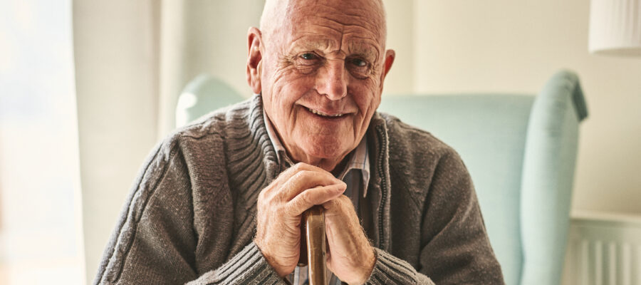 Portrait of happy senior man sitting at home with walking stock and smiling