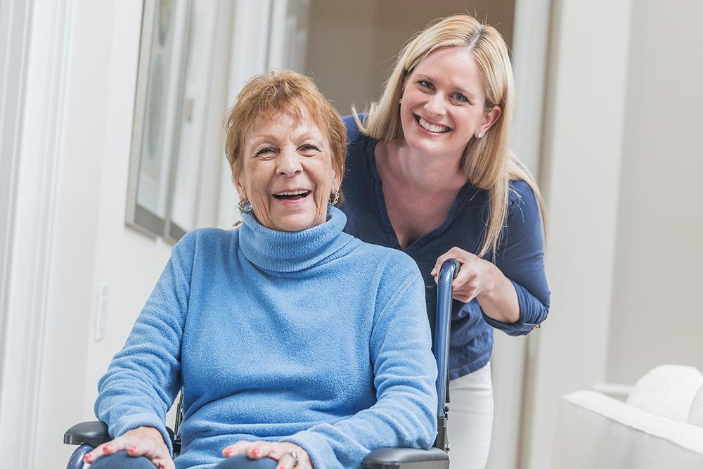 star-plus-program (unoptimized) elderly lady in wheelchair wearing blue long sleeve turtleneck sweater with contentedly happy smile (possibly laughing) with younger lady leaning into the picture wearing darker blue V-neck shirt smiling for the picture.