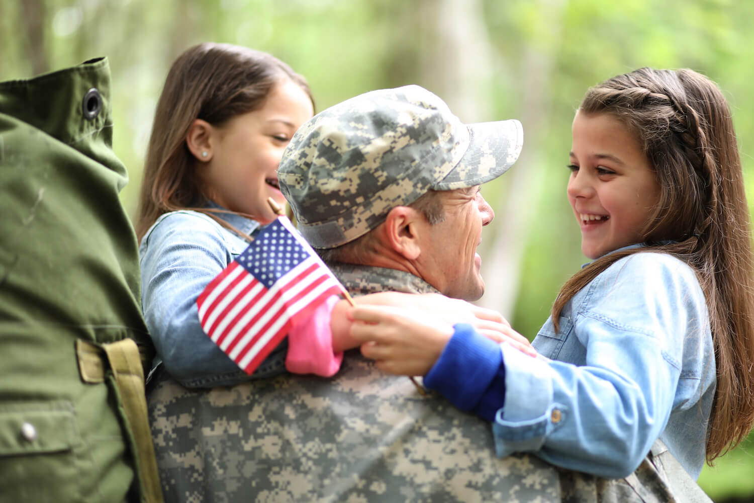 home_veteran-1 Family welcomes home a USA army soldier. The children excitedly hug father holding American flags.